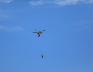 Fire fighting helicopter with waterbag on his way to combat the  fire