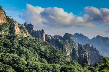 Lush green trees and sharp rocks slope from the top right down to the lower right corner in Huang Shan (黄山, Yellow Mountains) China