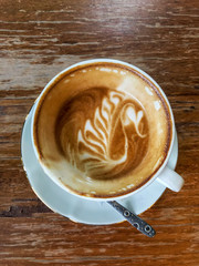 Latte art coffee  remain half of the white cup with spoon put on the wooden table and coppy space