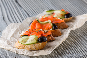 Bruschetta with smoked salmon, fresh cucumber, black olives and camembert on crumpled baking paper