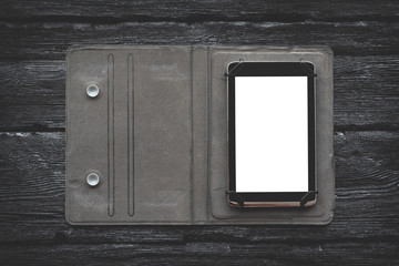 Digital tablet in case with a blank touch screen with a copy space on a black wooden table background.