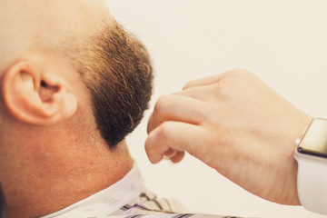 Fototapeta premium Bearded man, brutal, getting stylish hair shaving, haircut, with razor by barber or hairdresser at barbershop