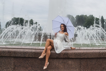 beautiful girl in white dress and umbrella by the fountain on a cloudy day