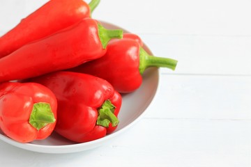 Fresh farm red bell pepper on a white plate on a light wooden background. Close-up.