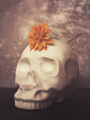 A yellow flower is in a gray vase. Behind is a gray bottle with a stopper in the form of a blue...