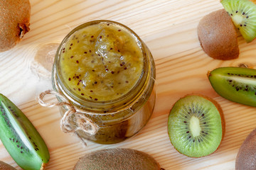 Top view of home preserving jar of kiwi homemade jam with raw tropical fruits on wooden background table in the kitchen. Healthy dessert snack recipes and veggie tables concept.