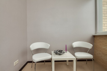 Interior design. Interior shots of a small balcony with white table and chairs near the gray empty clear wall and window.