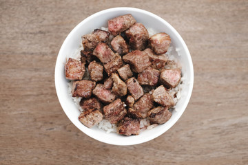 Homemade Bowl of Diced Beef Steak with rice Japanese style on wooden table.