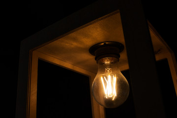 Close-up of warm yellow glowing light bulb encased in a wooden box against a black background