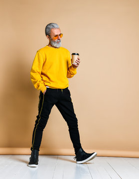 Vertical shot of a joyful senior holding a white coffee cup and looking at the camera