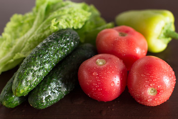 wet tomatoes, lettuce and cucumbers on dark wooden kitchen table	