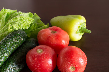 wet tomatoes, lettuce and cucumbers on dark wooden kitchen table	