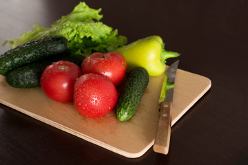 wet tomatoes, lettuce and cucumbers on dark wooden kitchen table	