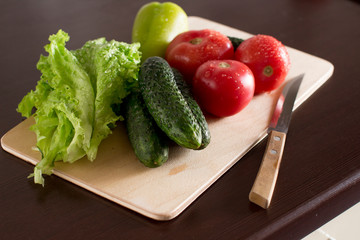 wet tomatoes, lettuce and cucumbers on dark wooden kitchen table	