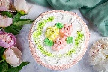 Beautiful delicious cake decorated with flowers in pastel colors on wooden table with peonies, top view