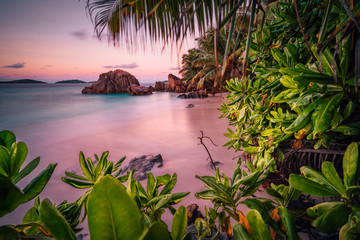 Beautiful romantic sunset sundown red sky on Seychelles paradise island. Granite rocks, palm trees and white sand beach - obrazy, fototapety, plakaty