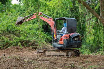 The man drive Backhoe clear nature for make the soil road in thailand