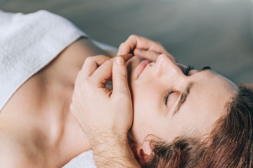 Male massage therapist makes face massage to a young beautiful woman.