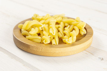 Lot of whole raw pasta gemelli on bamboo plate on white wood