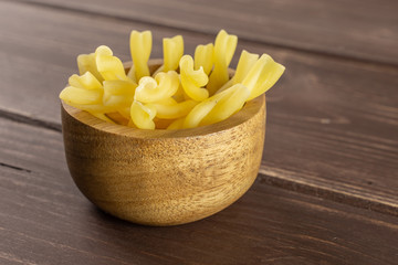 Lot of whole raw pasta gemelli in wooden bowl on brown wood