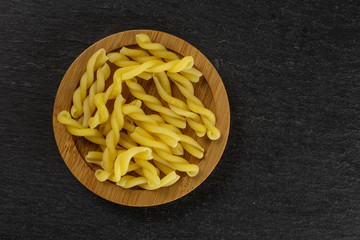 Lot of whole raw pasta gemelli on bamboo plate flatlay on grey stone