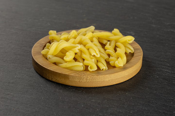 Lot of whole raw pasta gemelli on bamboo plate on grey stone