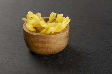 Lot of whole raw pasta gemelli in wooden bowl on grey stone