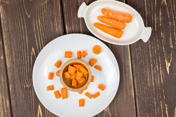 Group of three whole lot of pieces of stale  orange stale baby carrot baby on white porcelain plate flatlay isolated on brown wood