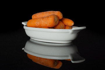 Lot of whole stale  orange stale baby carrot baby in a wooden bowl isolated on black glass