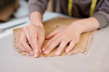 Young female tailor pinning paper workpiece to piece of fabric