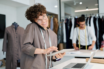 Happy female tailor consulting clients or taking orders by phone and online