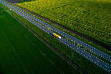 yellow truck driving on asphalt road along the green fields. seen from the air. Aerial view landscape. drone photography.  cargo delivery