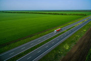 orange truck on the higthway sunset. cargo delivery driving on asphalt road along the green fields. seen from the air. Aerial view landscape. drone