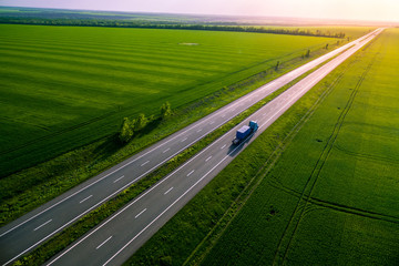 blue truck on the higthway sunset. cargo delivery driving on asphalt road along the green fields. seen from the air. Aerial view landscape. drone 