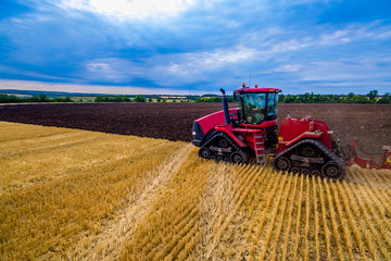 Obraz premium red tractor harrownig weat field. Aerial view. Farming