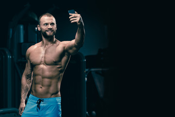 Fototapeta na wymiar Handsome smiling man with muscular fit body making selfie in gym