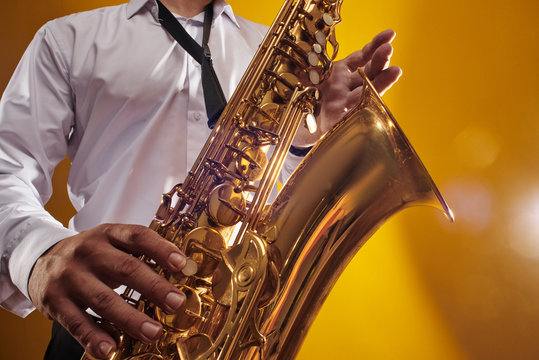 Portrait of professional musician saxophonist man in  white shirt plays jazz music on saxophone, yellow background in a photo studio, bottom view