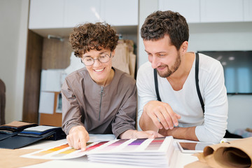 Two young happy fashion designers looking at one of color swatches in catalogue