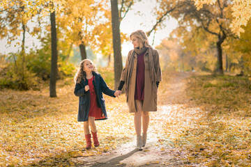 Young pretty mother with her little daughter having fun in the fall background. happy family with child daughter playing and laughing on autumn walk