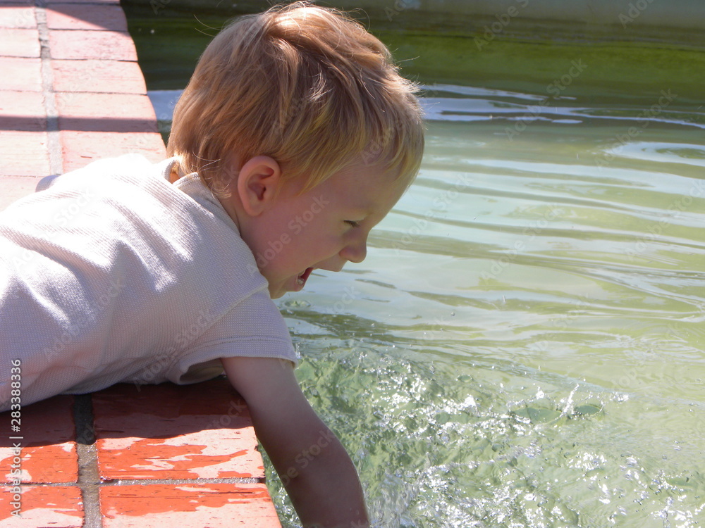 Wall mural little boy with blond hair plays with water