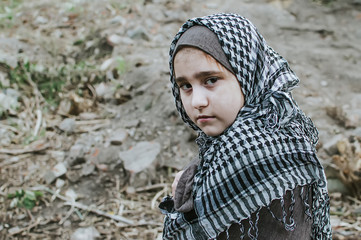 a refugee child in the war, a Muslim girl with a dirty face on the ruins, the concept of peace and...