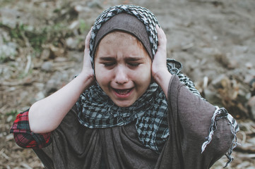 a refugee child in the war, a Muslim girl with a dirty face on the ruins, the concept of peace and war, the child is crying and waiting for help.