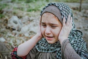 a refugee child in the war, a Muslim girl with a dirty face on the ruins, the concept of peace and war, the child is crying and waiting for help.