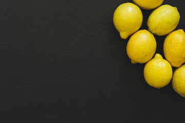 Group of bright yellow lemons in the right top corner on black background with copy space - Fresh tropical citrus fruits full of vitamins on dark slate