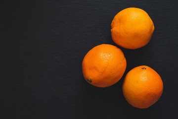 Whole oranges forming a triangle on a black background with copy space - Sweet citrus fruits on dark slate - Tropical ingredient in vegan diet
