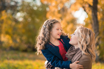 A portrait of a happy family: a young beautiful woman with her little cute daughter. Young daughter hugs mother in autumn colorful park outdoor. Mother's day