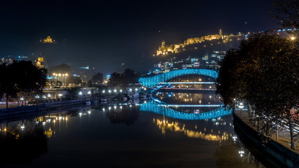 Fototapeta na wymiar Pedestrian bridge of peace over the Mtkvari (Kura) River in Tbilisi at night. Narikala fortress.