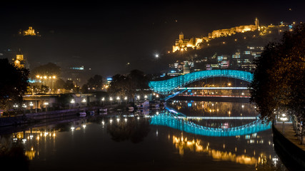 Fototapeta premium Pedestrian bridge of peace over the Mtkvari (Kura) River in Tbilisi at night. Narikala fortress.
