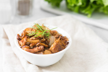 Fried chanterelles with onions in a white plate on a light gray table