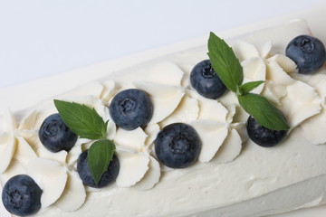 Sponge cake coated with cream and garnished with dried blueberries and fresh mint leaves.